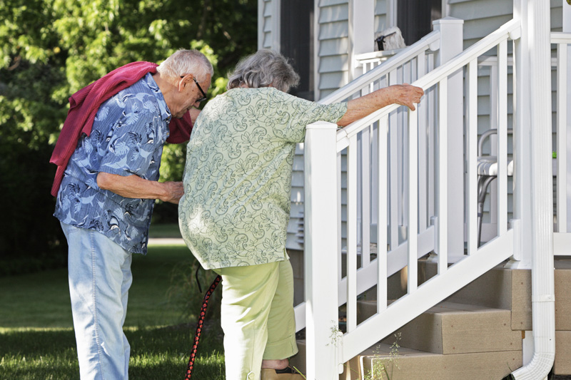 Elderly senior couple helping each other climb slowly up their back porch steps