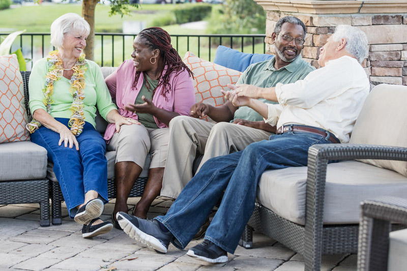 Group of older adults laughing and talking together on an outdoor patio in a senior living community.