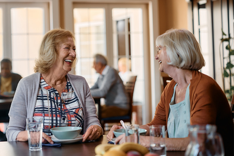 Older adults sharing a meal and laughing together at a restaurant-style dining table